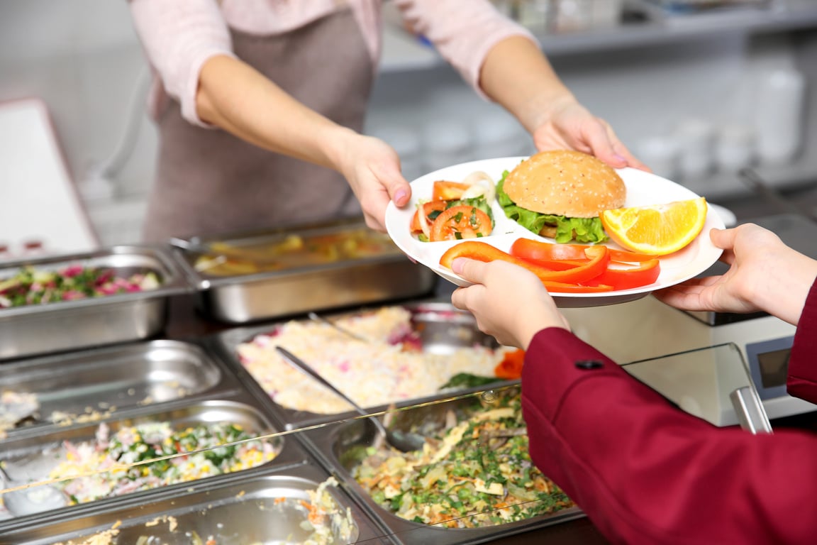 Woman Giving Lunch to School Girl in Cafeteria